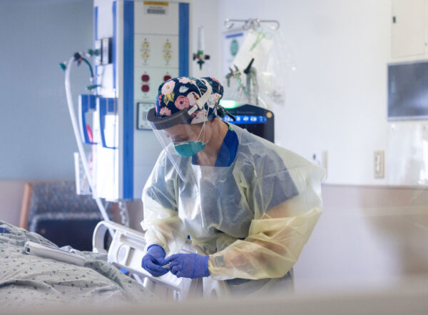 Nurse wearing full personal protective equipment bends over a patient bed in an ICU