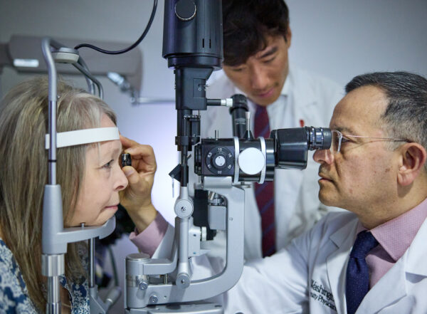 ophthalmologist examines patients eyes while medical student observes