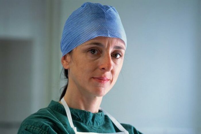 A woman wearing green scrubs and blue surgical cap looks at the camera