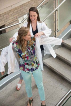 Second-year physical therapy student Gina Malito helps first-year student Elaina Stover into her white coat. 