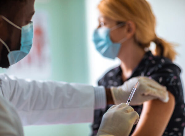 A woman wearing a mask prepares to receive a vaccination in her upper arm