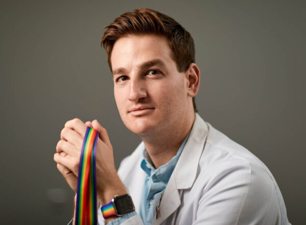Portrait of Cory French wearing a white coat and holding a rainbow lanyard