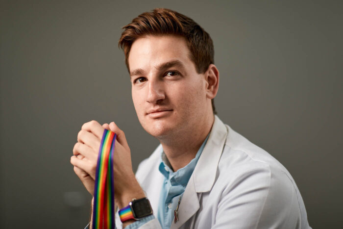 Portrait of Cory French wearing a white coat and holding a rainbow lanyard