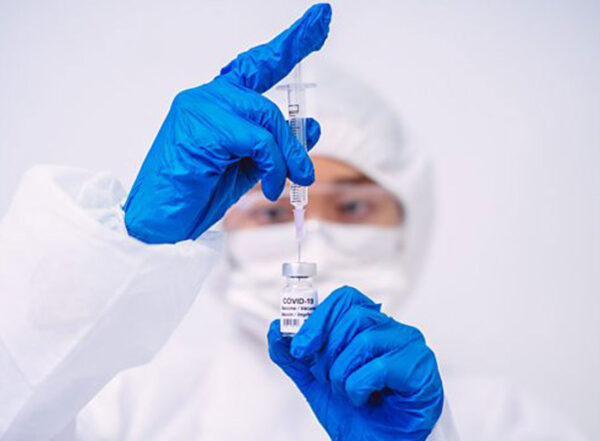 A person wearing PPE draws a vaccination dose from a small glass vial