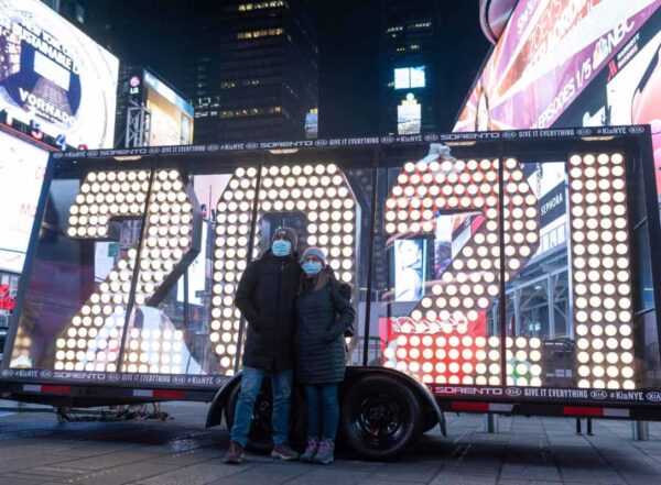People wearing masks takes a photo in front of the "2021" numbers that will replace the "2020" on the top of the One Times Square building near a "COVID-19 safety guidelines" sign in Times Square
