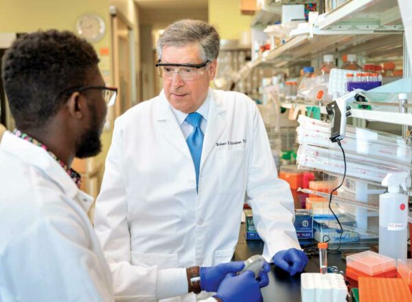 Robert D. Schreiber, PhD, right, consults with doctoral student Samuel O. Ameh in a lab.