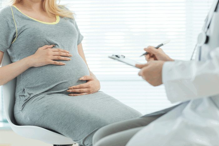 Pregnant woman in gray dress talking to doctor in white coat